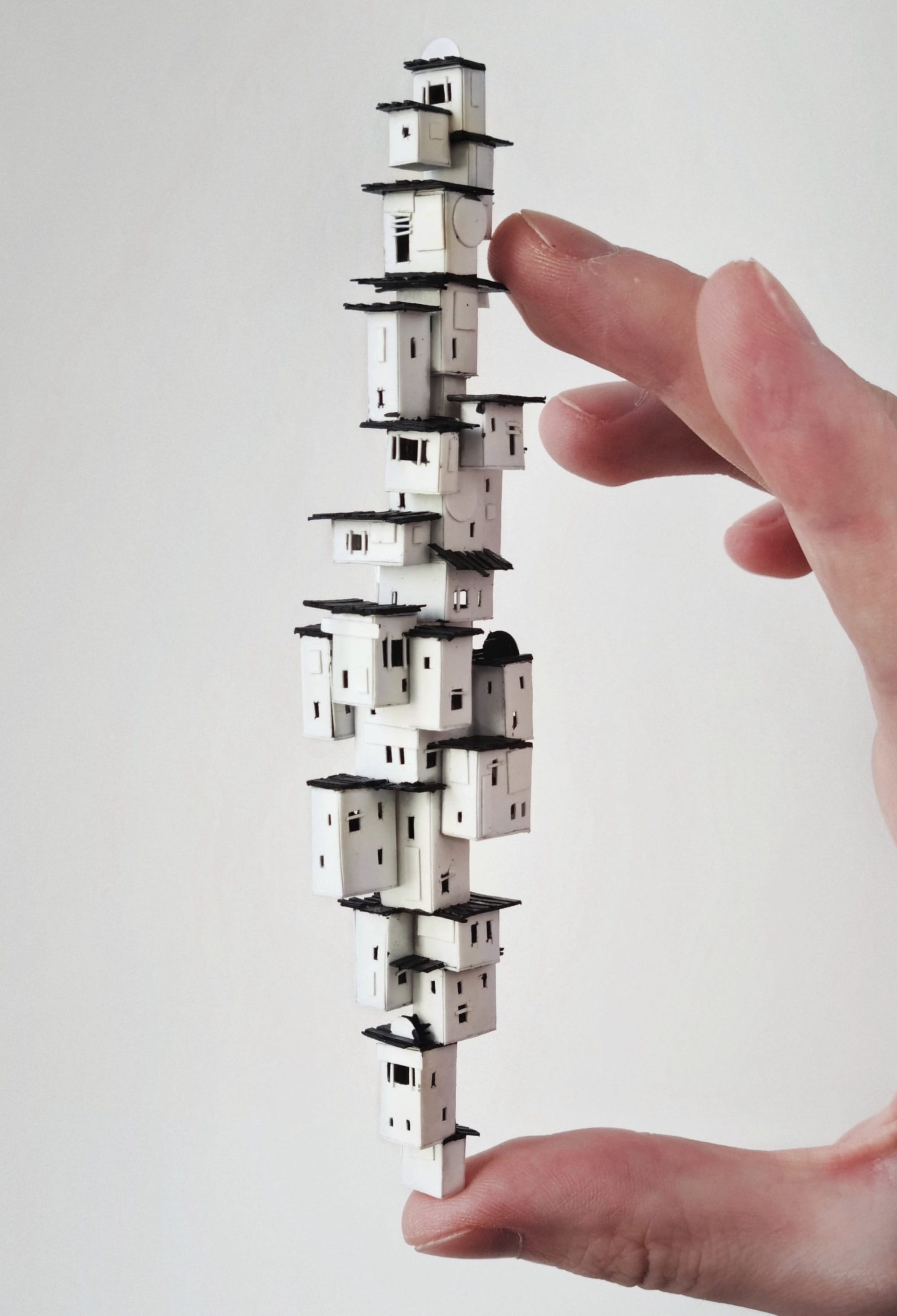 a hand holds a tiny vertical sculpture of stacked white houses, by Michael Davydov