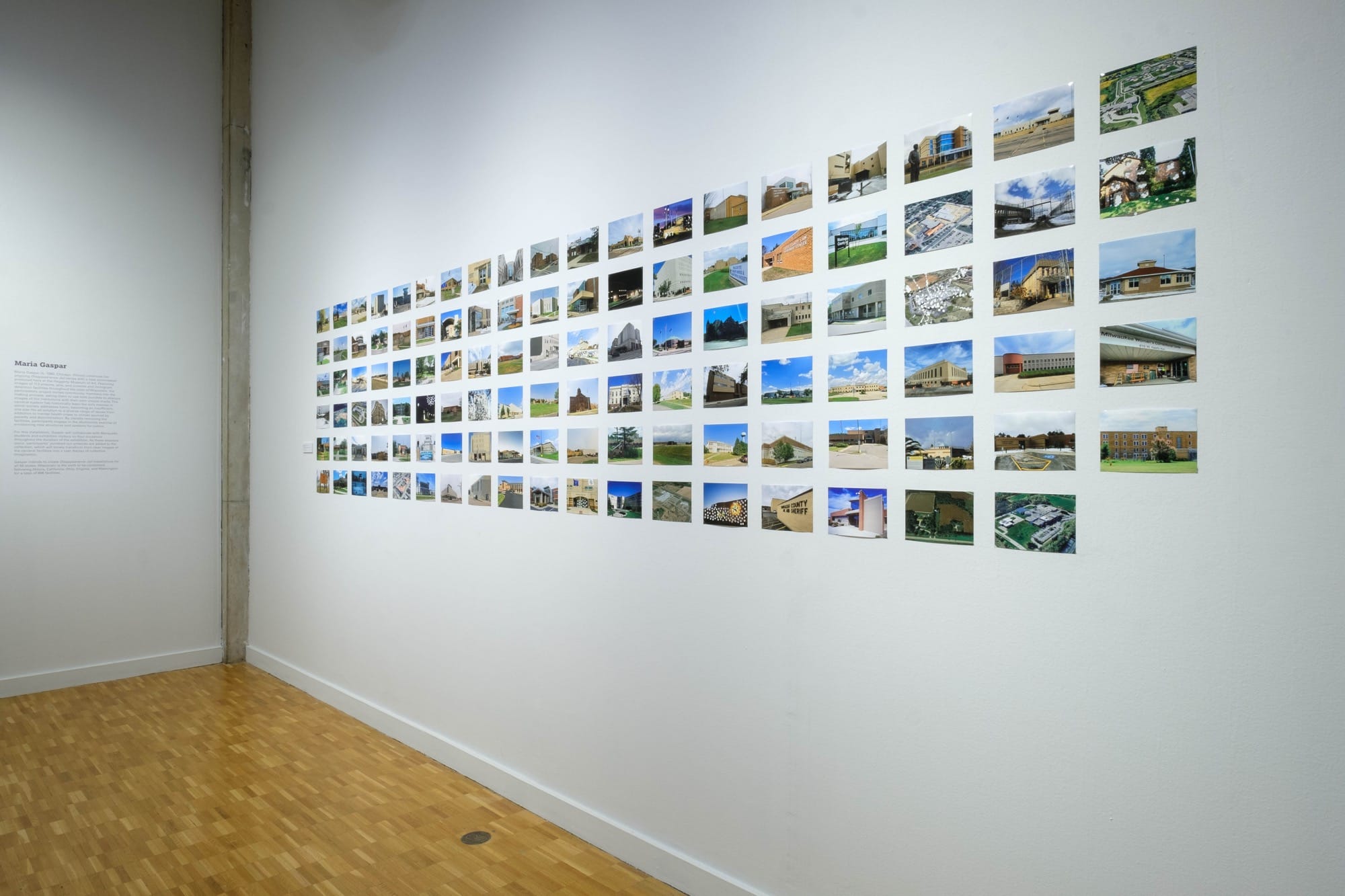 a grid of photos of buildings. some are riddled with hole punches in a view of an installation by Maria Gaspar in a gallery at the Haggerty Museum of Art