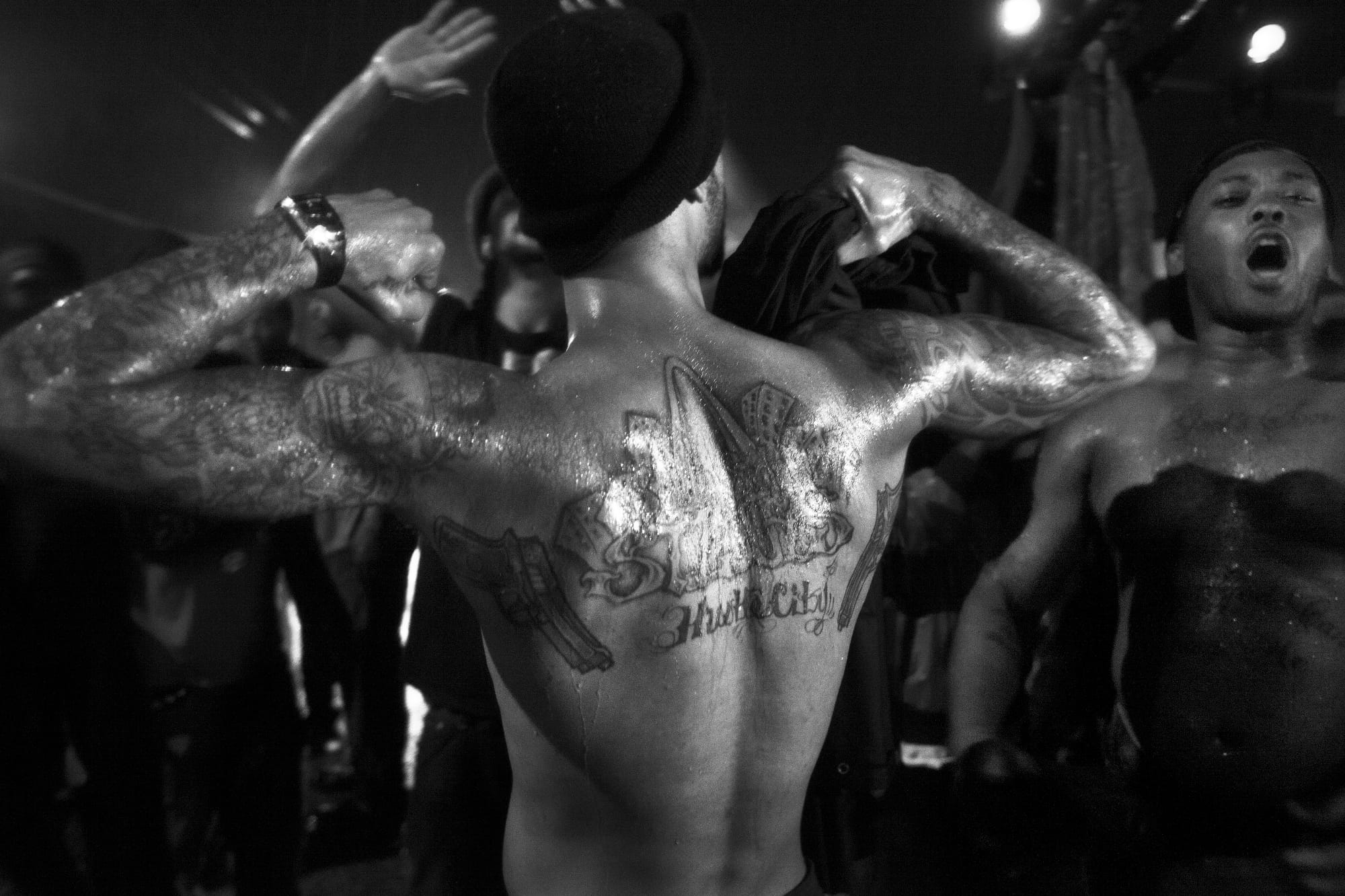 A black-and-white photograph by Carlos Javier Ortiz of demonstrators in St. Louis, with a focus on one man's bare back with a large tattoo