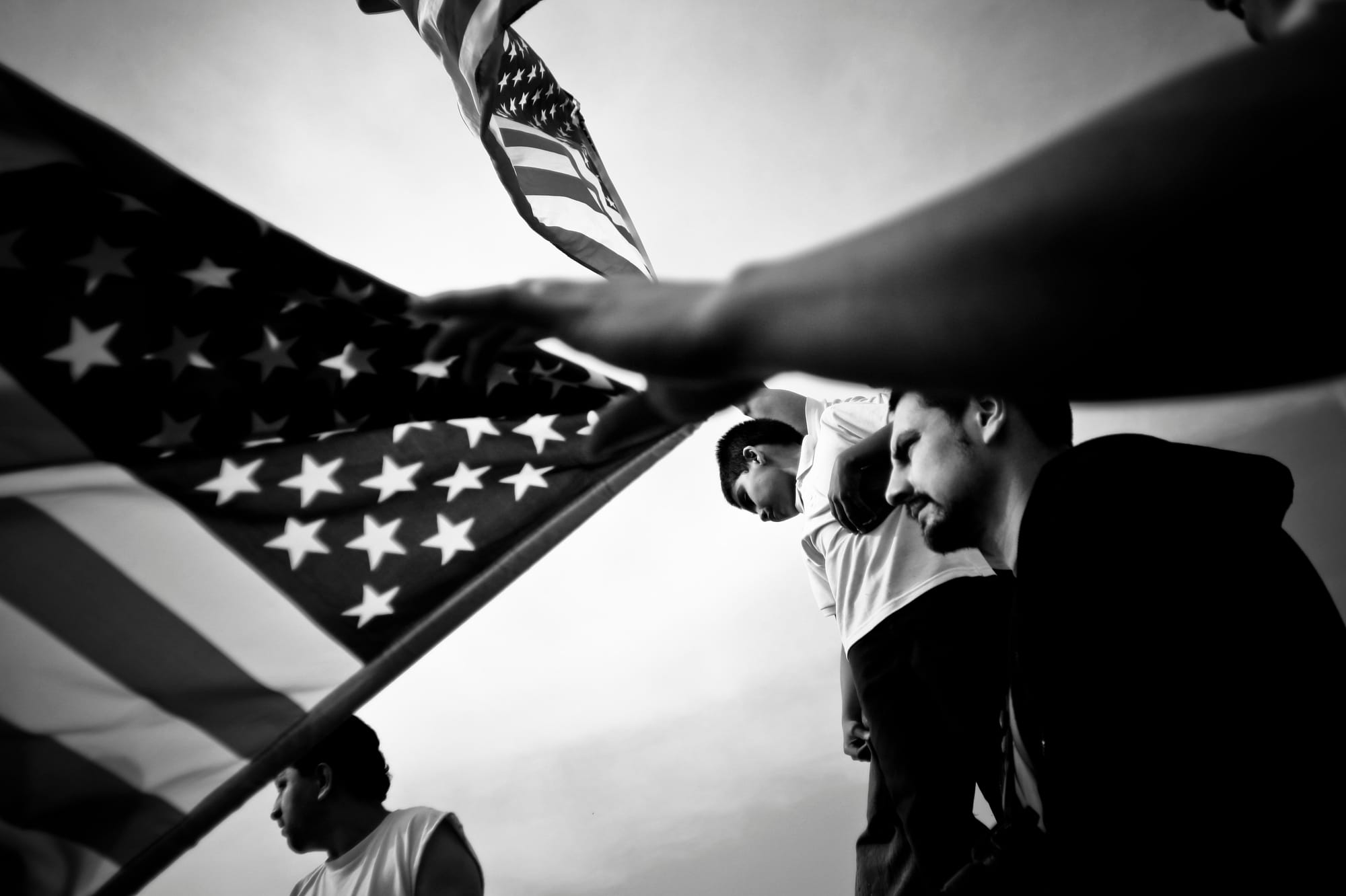 A black-and-white photograph by Carlos Javier Ortiz of demonstrators walking with the American flag