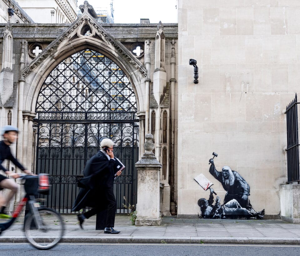 a barrister walks by the Royal Courts of London, where a spraypainted image by Banksy on the wall depicts a judget violently attacking a pro-Palestine protestor