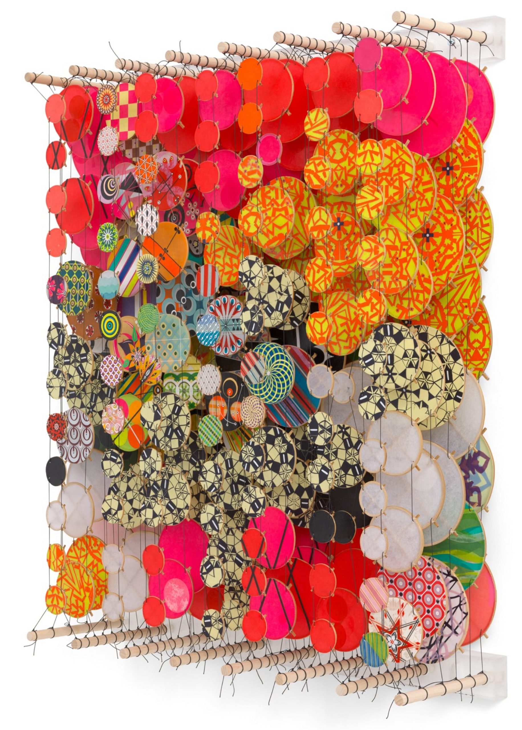 an oblique view of an abstract artwork by Jacob Hashimoto made from twine and numerous colorful, patterned paper discs installed in rows for a layered effect
