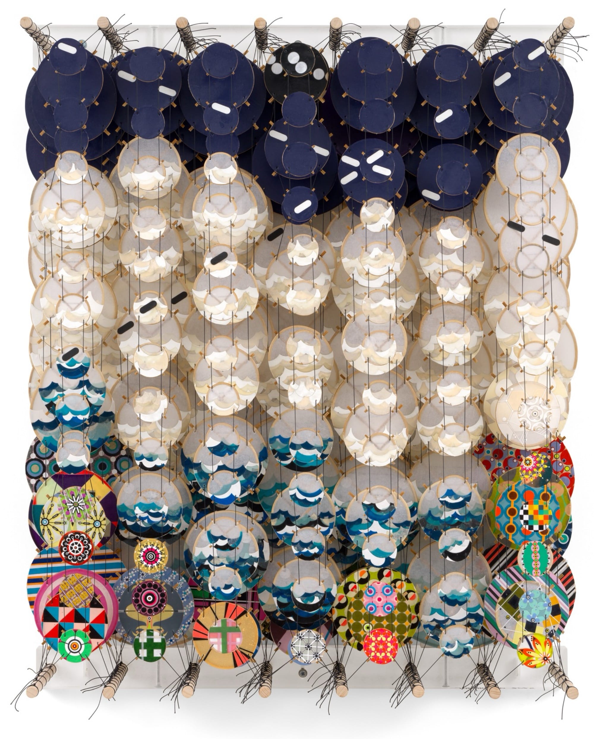 an abstract artwork by Jacob Hashimoto made from twine and numerous colorful, patterned paper discs installed in rows for a layered effect