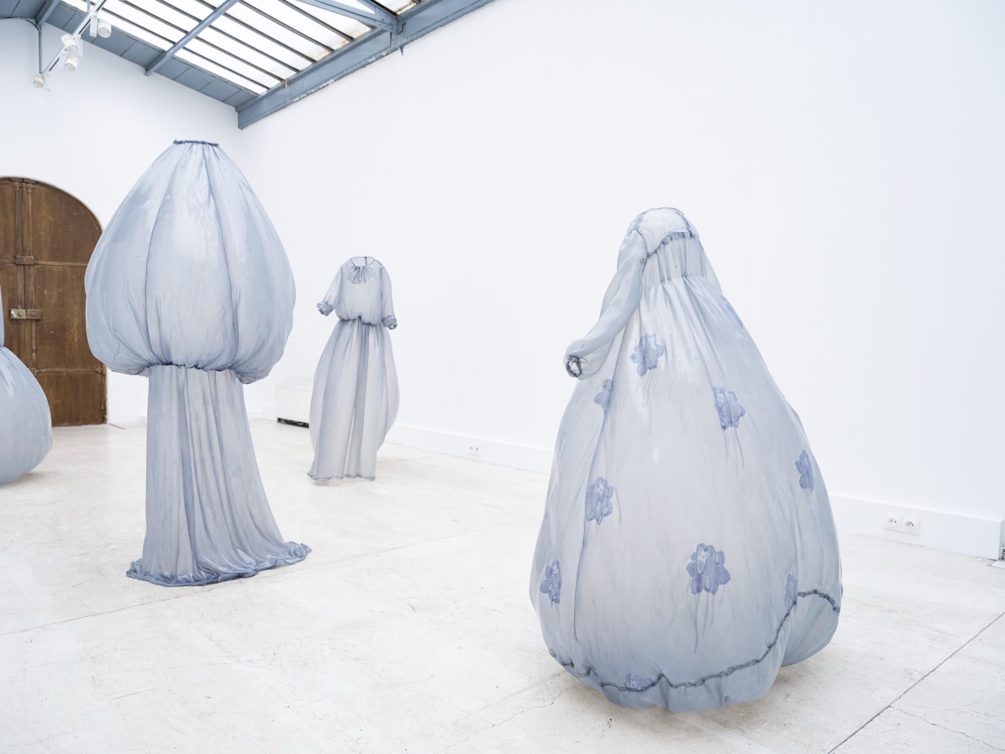 a collection of stiff pale blue fiberglass victorian style dresses by Brandon Morris that stand without wearers in the middle of a gallery