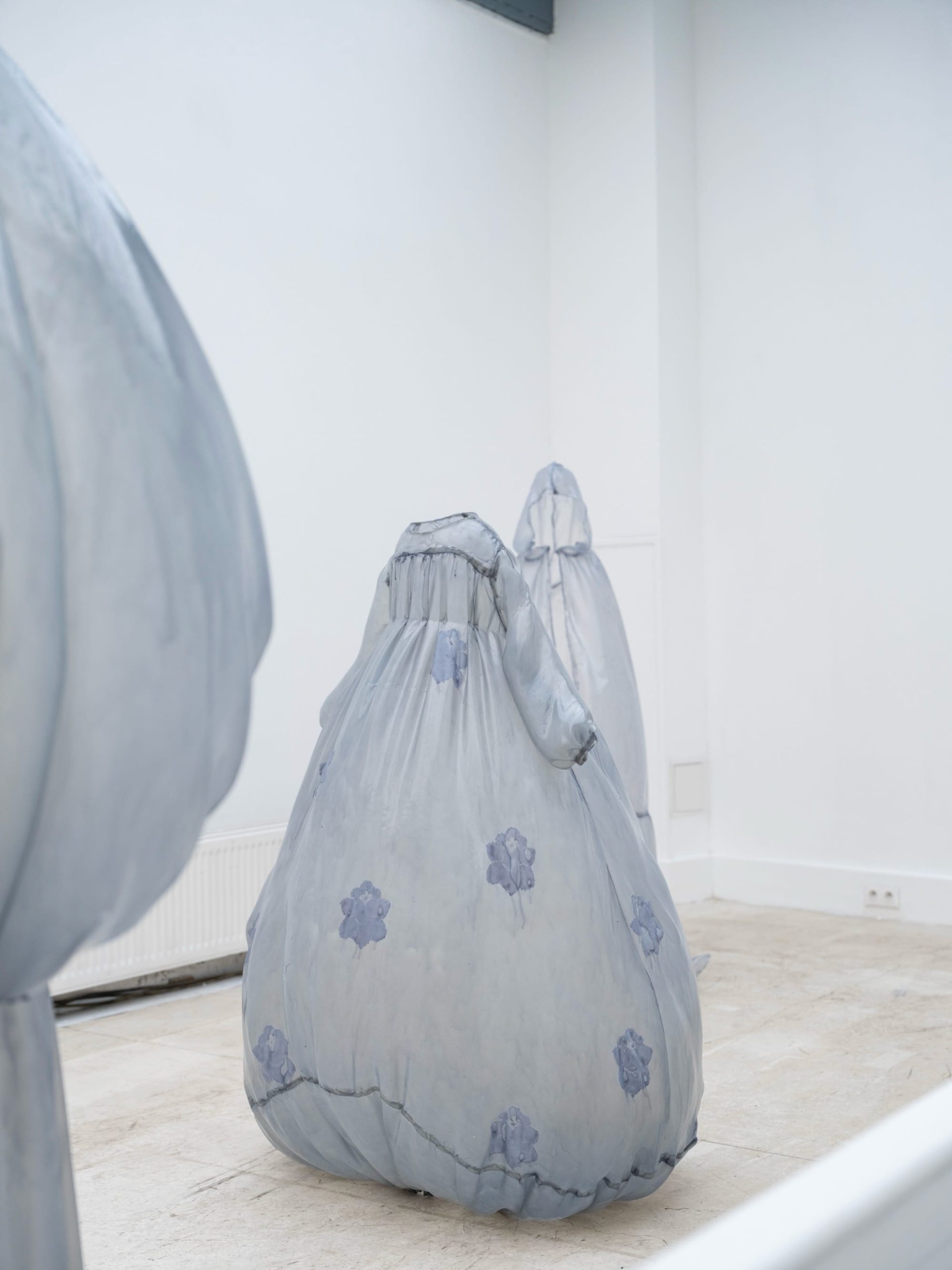 a collection of stiff pale blue fiberglass victorian style dresses by Brandon Morris that stand without wearers in the middle of a gallery